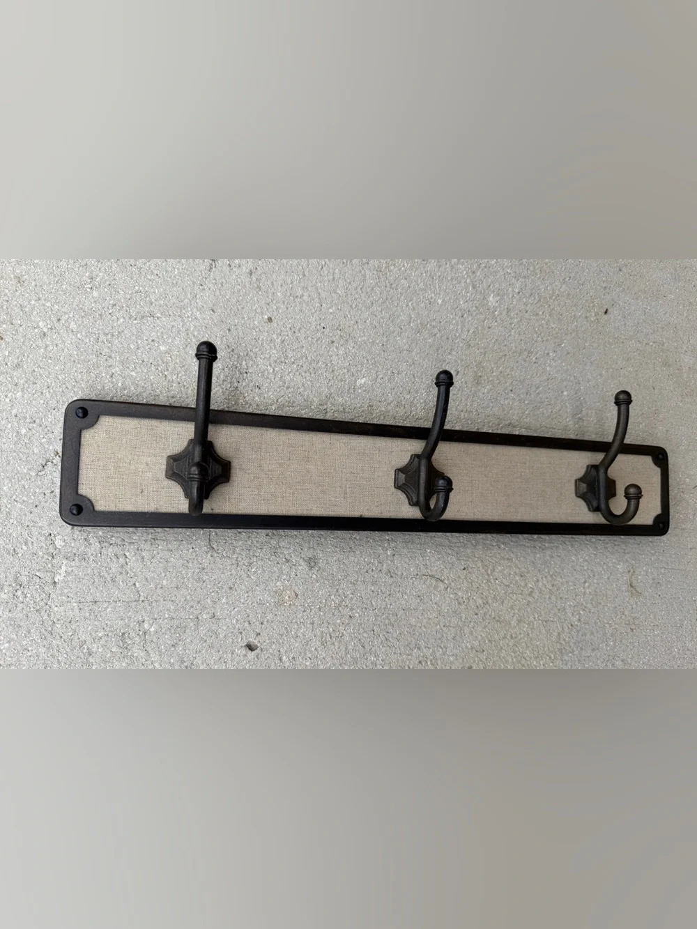Hook rack features a dark bronze frame with a light-colored linen backing